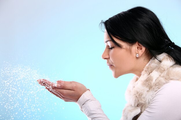 A woman dressed in winter clothing blowing snowflakes from her hands, symbolizing cold weather, respiratory health, immunity, and seasonal healthcare.
