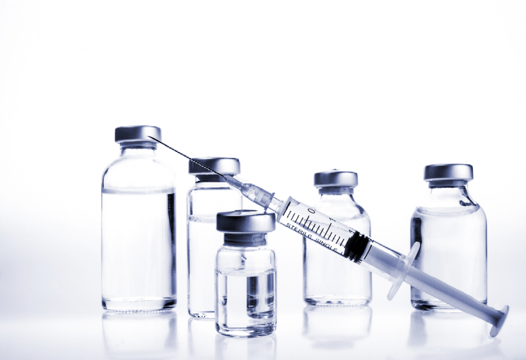 Syringe and sealed medication vials on a clean white background.