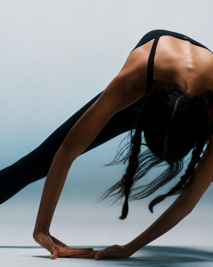 Woman performing a deep yoga stretch in black activewear against a minimalist studio background.