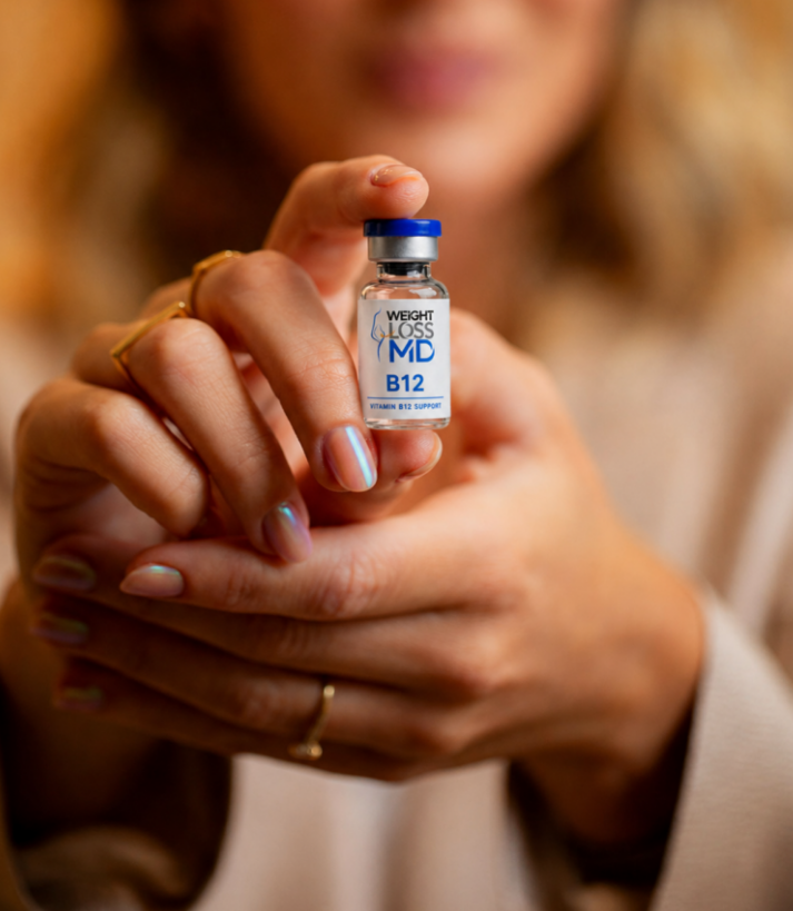Woman holding a Weight Loss MD Vitamin B12 injection vial toward the camera in a professional wellness setting.