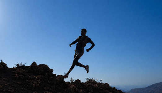 Silhouetted runner jumping across rocky terrain against a deep blue sky