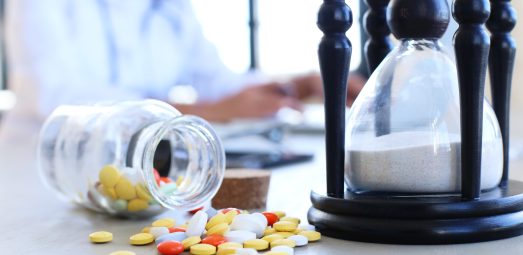 "Prescription pills spilled from a bottle next to an hourglass, symbolizing time-sensitive healthcare treatments and medication adherence."